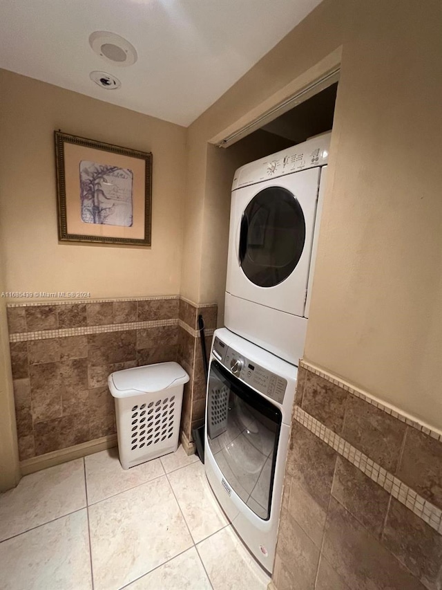 washroom with stacked washer and dryer, light tile patterned floors, and tile walls