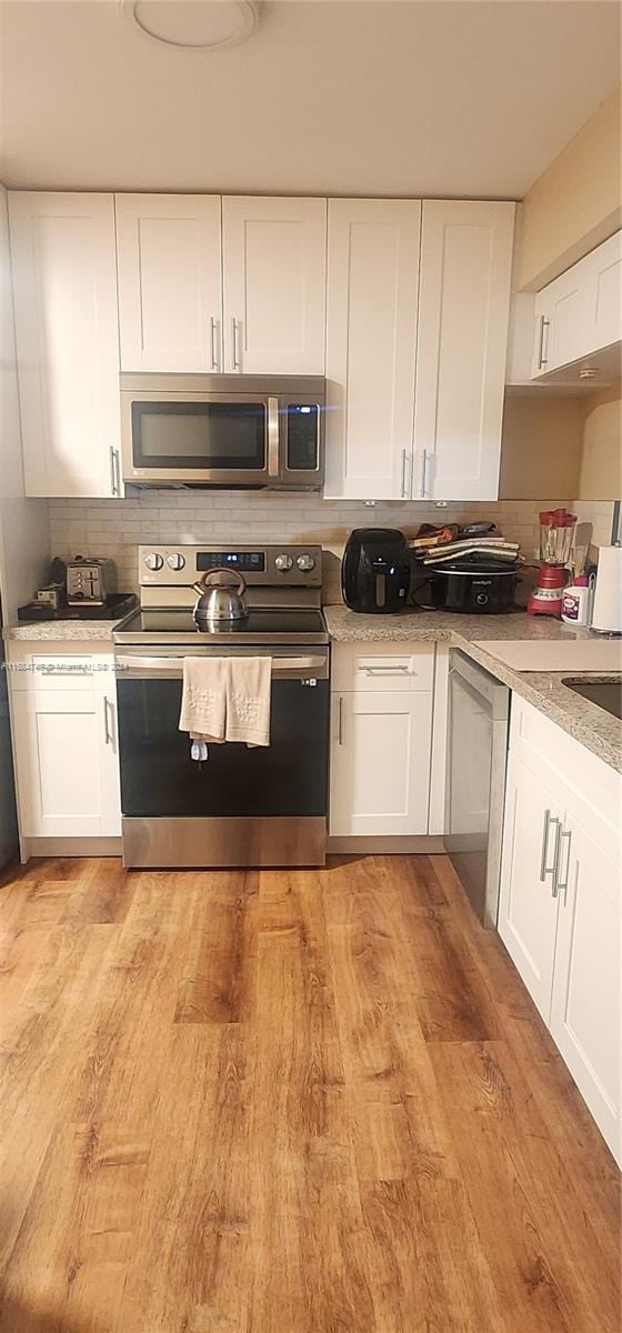 kitchen with light hardwood / wood-style floors, decorative backsplash, white cabinets, and stainless steel appliances