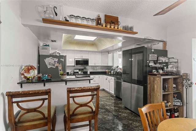 kitchen featuring sink, a textured ceiling, kitchen peninsula, stainless steel appliances, and white cabinets