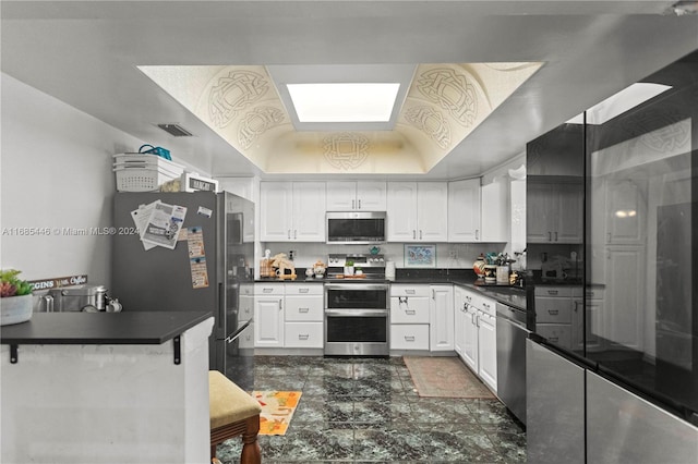 kitchen with stainless steel appliances, vaulted ceiling, and white cabinets