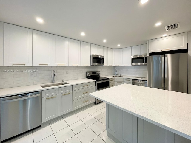 kitchen with appliances with stainless steel finishes, light tile patterned flooring, light stone countertops, and sink