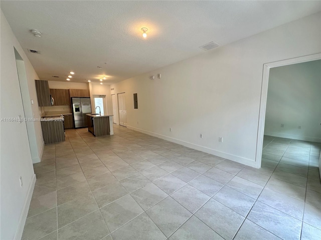 kitchen featuring a center island with sink, a textured ceiling, light tile patterned flooring, stainless steel refrigerator with ice dispenser, and sink