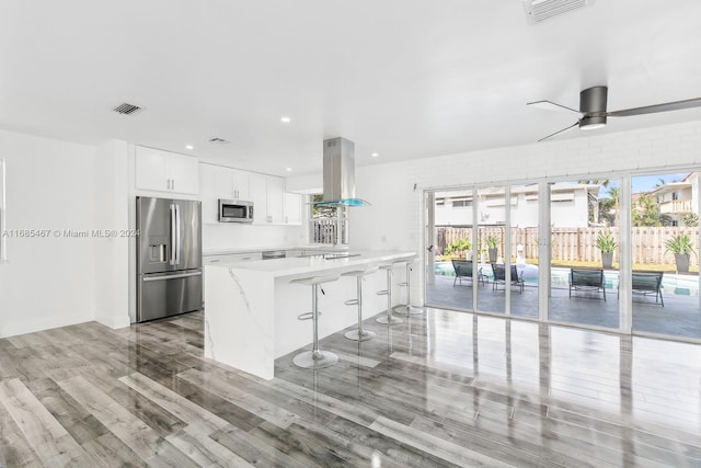 kitchen featuring island exhaust hood, white cabinetry, stainless steel appliances, and a wealth of natural light