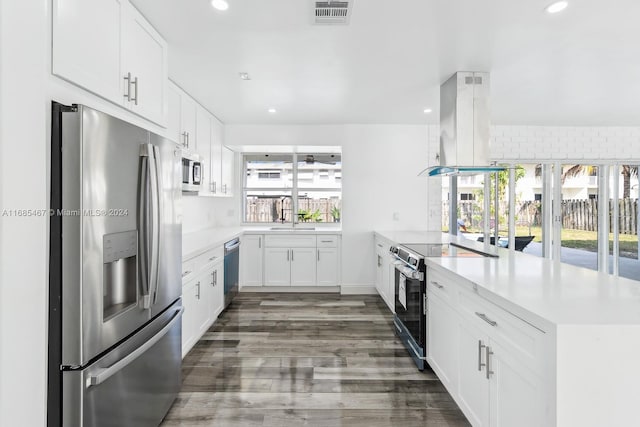 kitchen with dark wood-type flooring, island exhaust hood, stainless steel appliances, and white cabinets