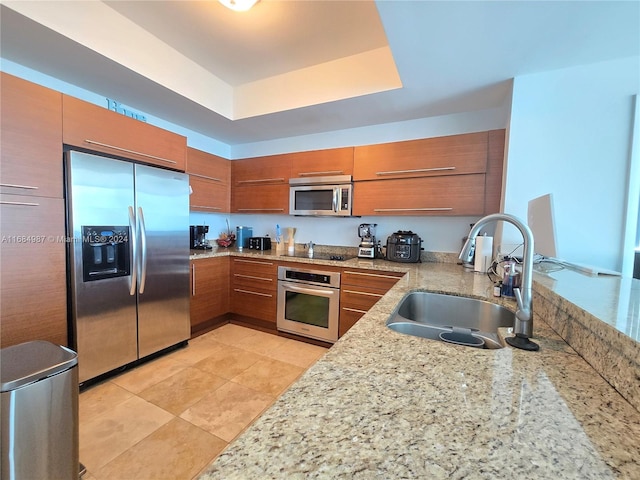 kitchen with stainless steel appliances, sink, kitchen peninsula, light stone counters, and a raised ceiling