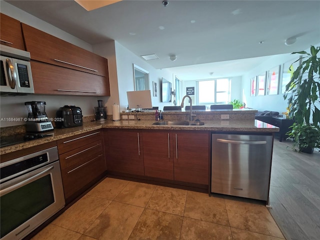 kitchen with sink, kitchen peninsula, appliances with stainless steel finishes, dark stone counters, and light wood-type flooring