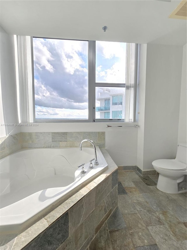 bathroom featuring toilet, a wealth of natural light, and tiled tub