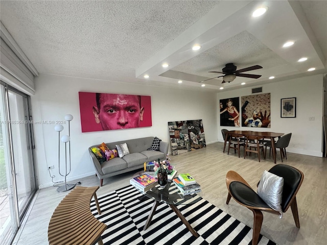 living room featuring a textured ceiling, ceiling fan, light wood-type flooring, and a raised ceiling