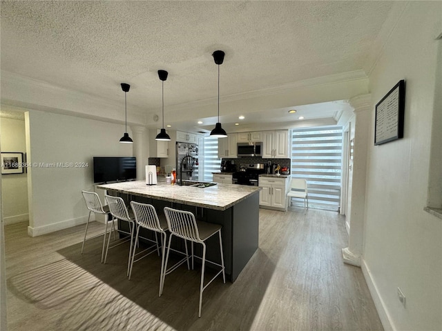 kitchen with a large island with sink, white cabinetry, sink, pendant lighting, and stainless steel appliances