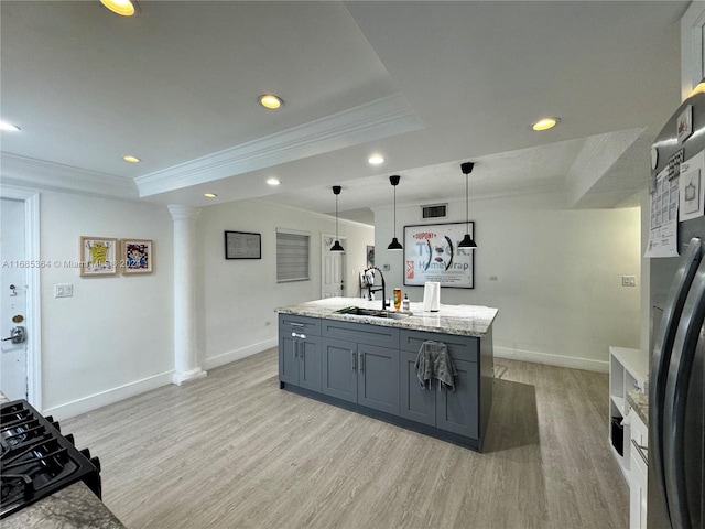 kitchen featuring sink, light wood-type flooring, a raised ceiling, decorative light fixtures, and a kitchen island with sink