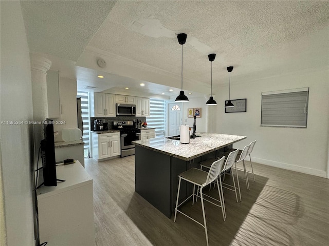 kitchen with light wood-type flooring, a center island, white cabinetry, stainless steel appliances, and pendant lighting