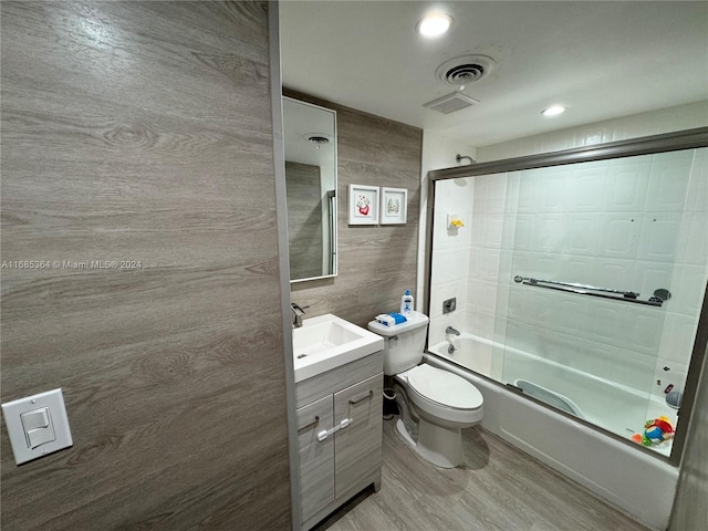 full bathroom featuring hardwood / wood-style floors, combined bath / shower with glass door, tile walls, toilet, and vanity