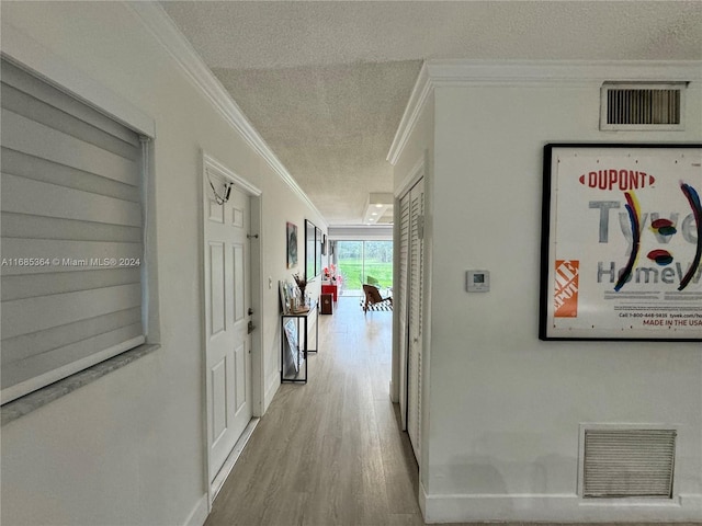 corridor with ornamental molding, light hardwood / wood-style flooring, and a textured ceiling