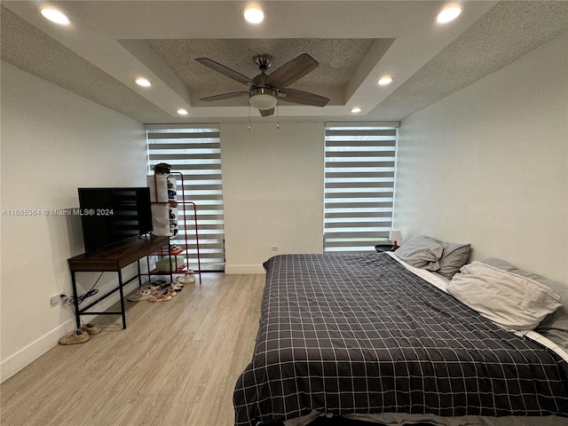 bedroom featuring ceiling fan, a raised ceiling, wood-type flooring, and a textured ceiling