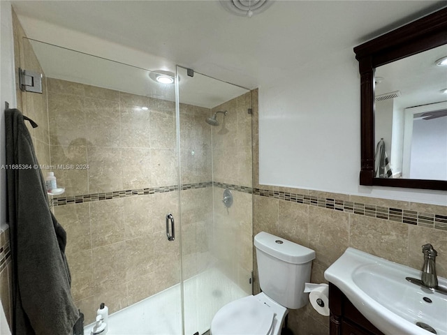 bathroom featuring tile walls, vanity, a shower with shower door, and toilet