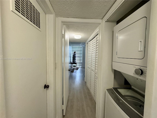 washroom with light hardwood / wood-style floors, stacked washing maching and dryer, and a textured ceiling