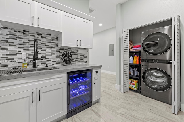 laundry area with wine cooler, stacked washer and dryer, a sink, wet bar, and laundry area