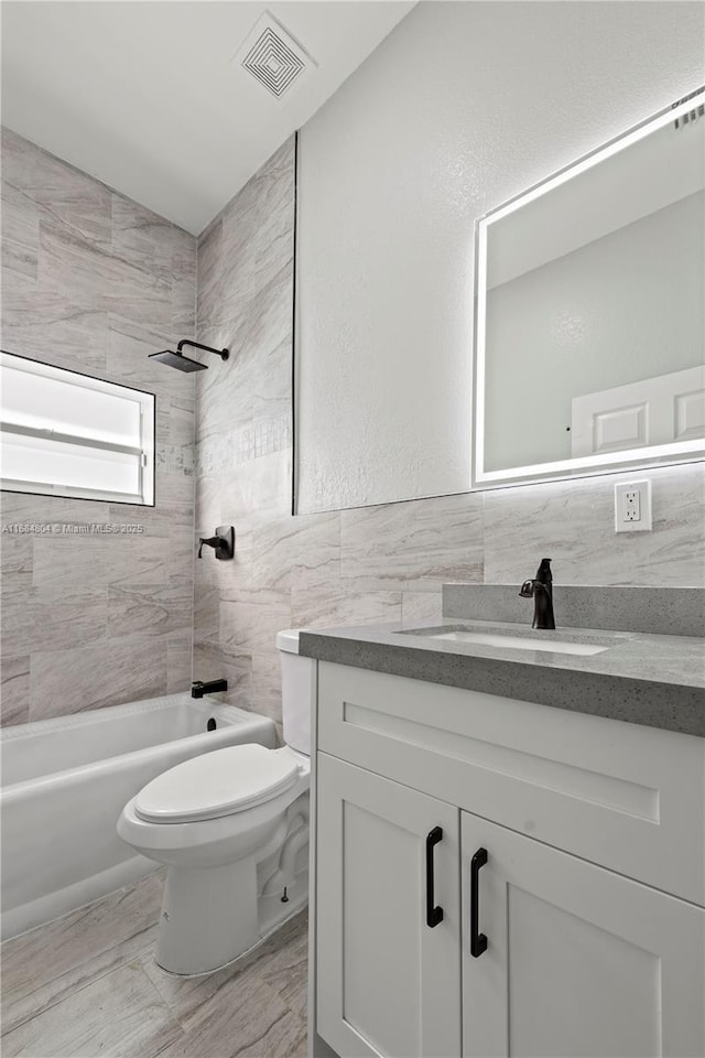 bathroom with toilet, bathing tub / shower combination, vanity, visible vents, and tile walls