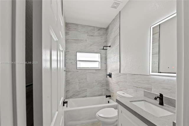 bathroom with tile walls, visible vents, toilet, tub / shower combination, and vanity