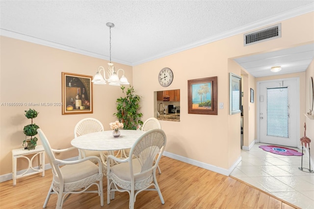 dining room featuring a notable chandelier, light hardwood / wood-style flooring, a textured ceiling, and ornamental molding