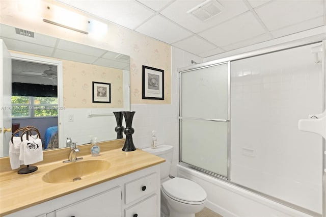 full bathroom with a paneled ceiling, vanity, toilet, enclosed tub / shower combo, and tile walls