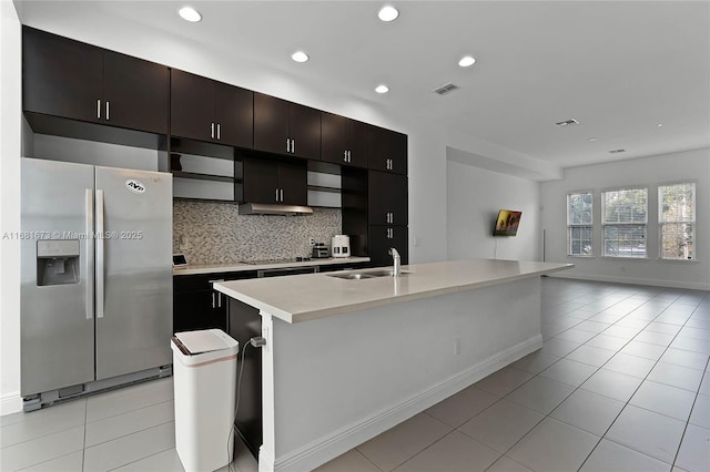 kitchen featuring sink, backsplash, light tile patterned floors, stainless steel refrigerator with ice dispenser, and a center island with sink