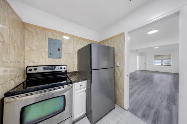 kitchen with white cabinetry, stainless steel appliances, electric panel, light hardwood / wood-style floors, and tile walls