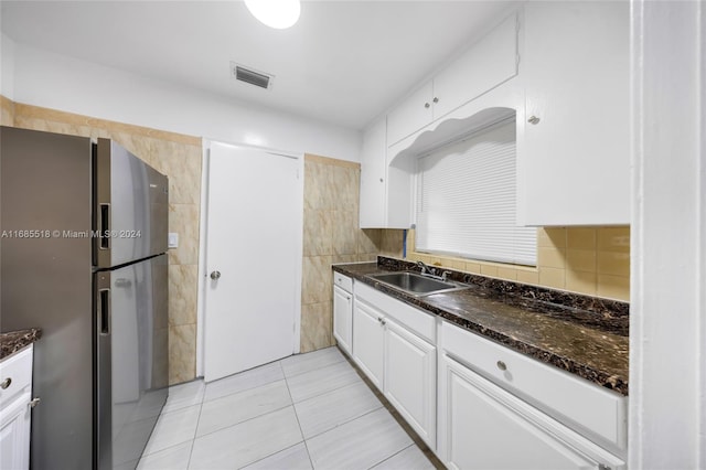 kitchen with sink, light tile patterned floors, stainless steel fridge, dark stone counters, and white cabinets