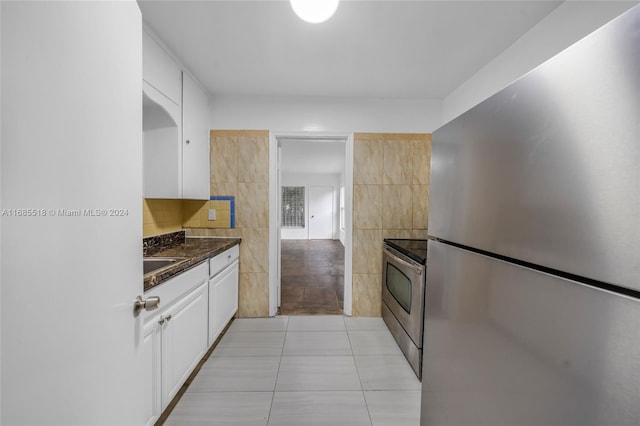 kitchen with dark stone counters, stainless steel appliances, light tile patterned floors, tile walls, and white cabinets