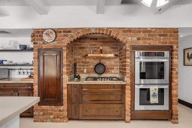 kitchen with brick wall, appliances with stainless steel finishes, and beam ceiling