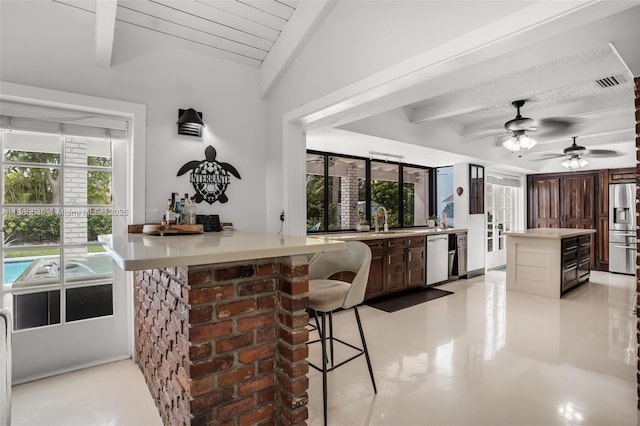 kitchen with beam ceiling, dark brown cabinets, stainless steel appliances, and a healthy amount of sunlight