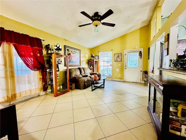 living area featuring vaulted ceiling, ceiling fan, plenty of natural light, light tile patterned floors, and a textured ceiling