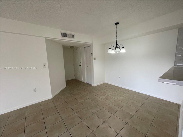 spare room featuring a chandelier, a textured ceiling, and tile patterned flooring