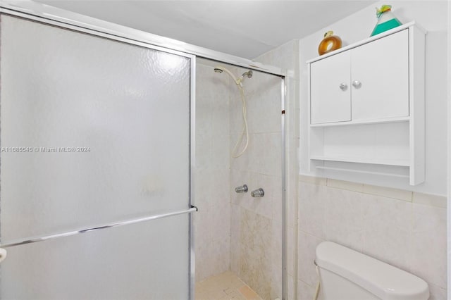 bathroom featuring a shower with door, toilet, and tile walls