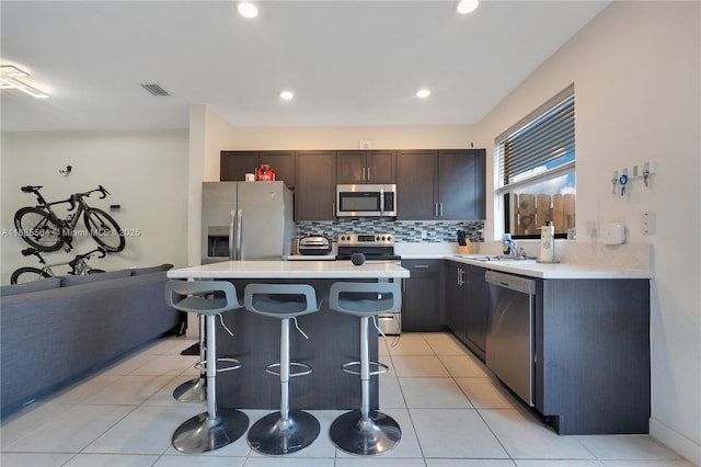 kitchen featuring stainless steel appliances, a kitchen island, a breakfast bar, light tile patterned flooring, and dark brown cabinets