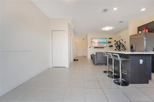 kitchen with a kitchen bar, light tile patterned floors, stainless steel refrigerator with ice dispenser, and kitchen peninsula