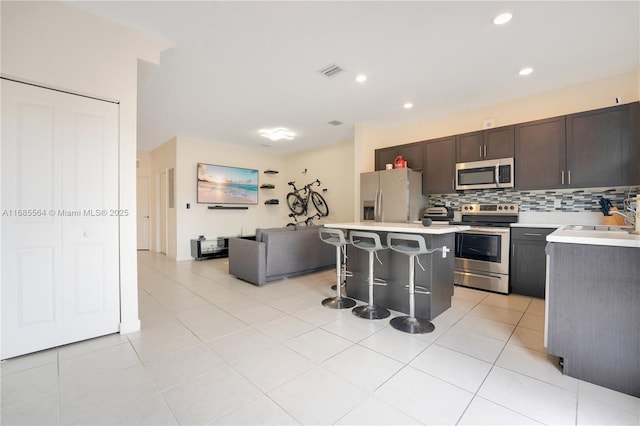 kitchen with appliances with stainless steel finishes, sink, light tile patterned floors, a center island, and a breakfast bar area