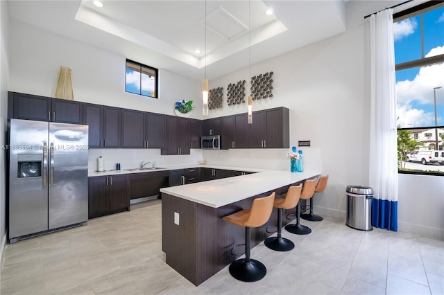 kitchen featuring a breakfast bar, a raised ceiling, sink, appliances with stainless steel finishes, and kitchen peninsula