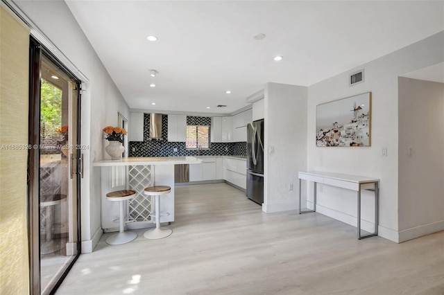 kitchen featuring a kitchen bar, kitchen peninsula, stainless steel fridge, light hardwood / wood-style floors, and white cabinets