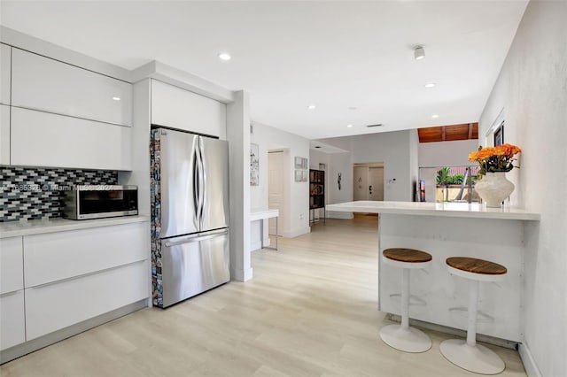 kitchen featuring tasteful backsplash, a kitchen bar, light wood-type flooring, white cabinetry, and stainless steel appliances