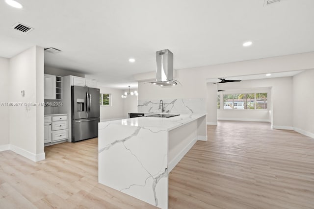 kitchen featuring island range hood, stainless steel refrigerator with ice dispenser, kitchen peninsula, light stone countertops, and white cabinets