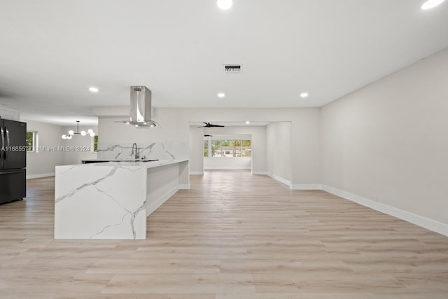 kitchen with hanging light fixtures, island range hood, black refrigerator, light hardwood / wood-style floors, and light stone counters