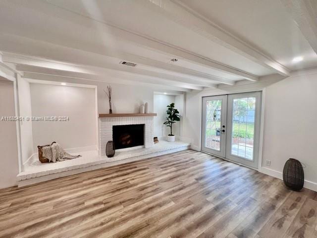 unfurnished living room with beam ceiling, a brick fireplace, french doors, and hardwood / wood-style flooring