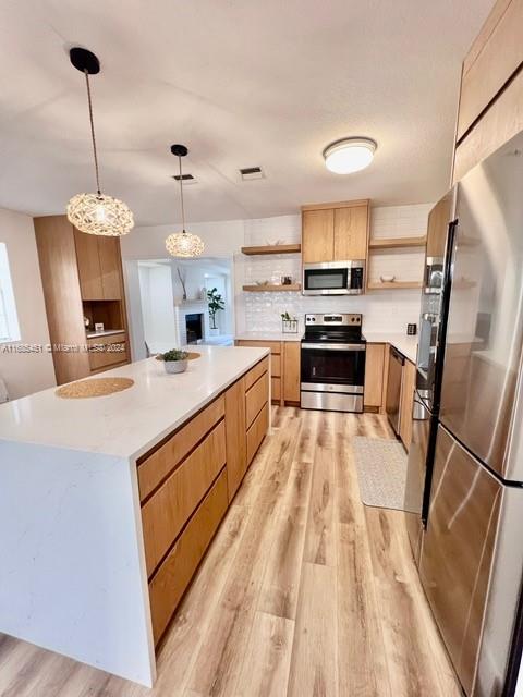 kitchen with pendant lighting, decorative backsplash, light hardwood / wood-style floors, appliances with stainless steel finishes, and a kitchen island