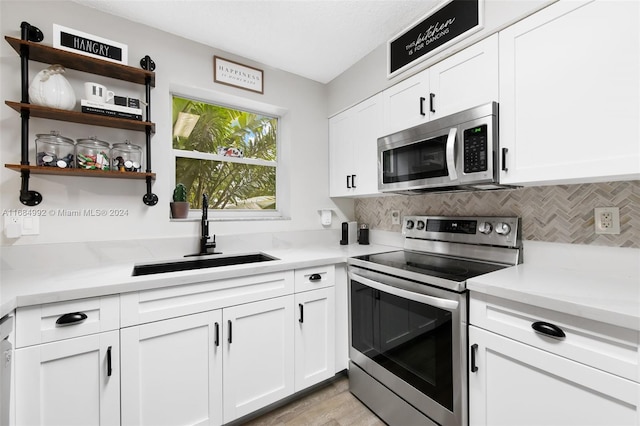 kitchen with sink, backsplash, light hardwood / wood-style floors, stainless steel appliances, and white cabinets