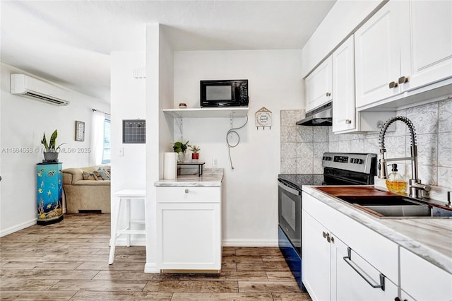 kitchen with sink, electric range, a wall unit AC, and white cabinets