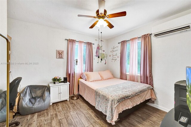 bedroom with ceiling fan, a wall mounted air conditioner, hardwood / wood-style floors, and multiple windows