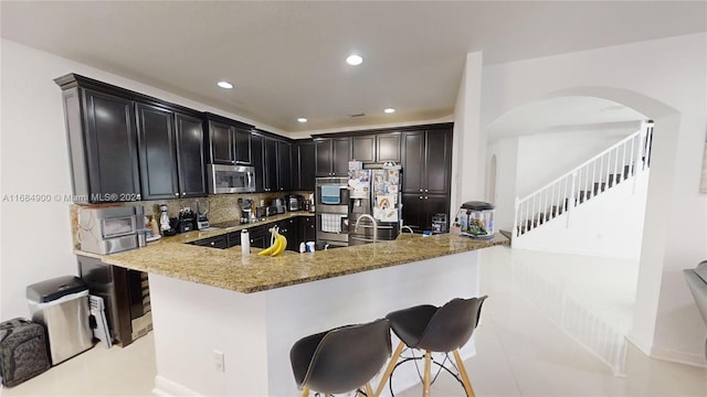 kitchen with backsplash, light stone counters, kitchen peninsula, and stainless steel appliances