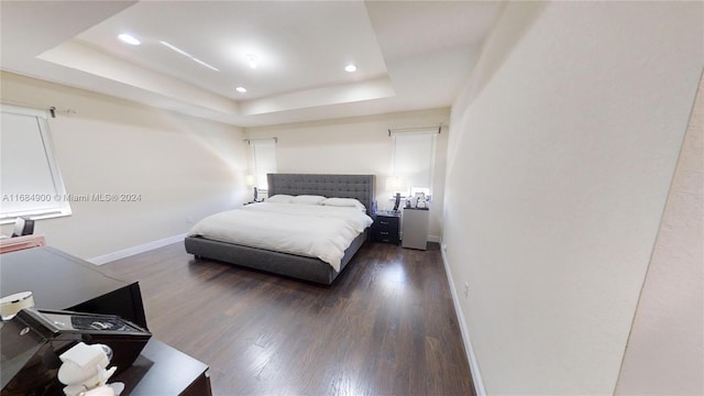 bedroom with a raised ceiling and dark wood-type flooring