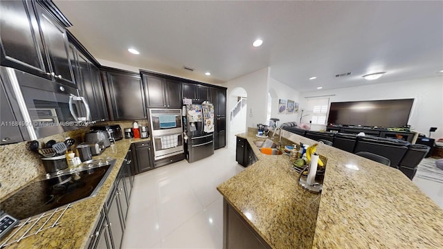 kitchen featuring backsplash, light stone counters, light tile patterned floors, and appliances with stainless steel finishes